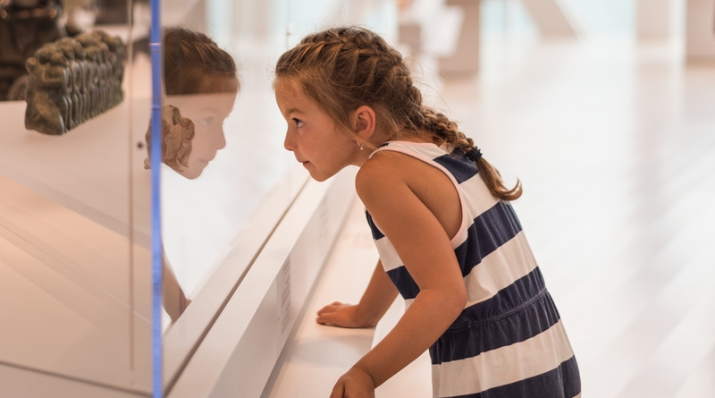 Enfant face à une vitrine d’exposition dans un musée.