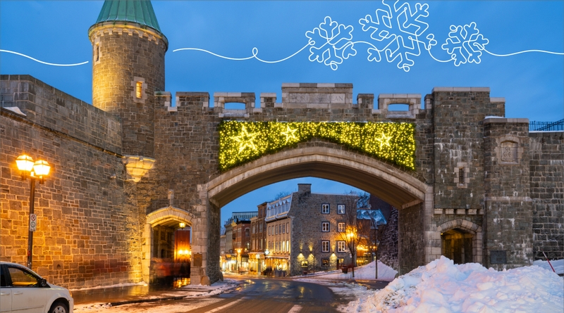 Porte fortifiée en pierre du Vieux-Québec, ornée d’une guirlande lumineuse en forme d’étoile pour les décorations hivernales. La scène se déroule au crépuscule, avec un ciel bleu et des lampadaires allumés. On aperçoit des bâtiments historiques à travers 
